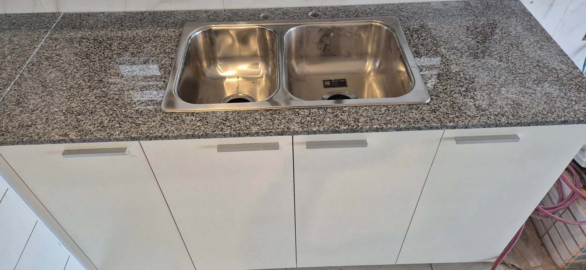 Mesada de granito con bacha doble de acero y muebles bajo mesada blancos